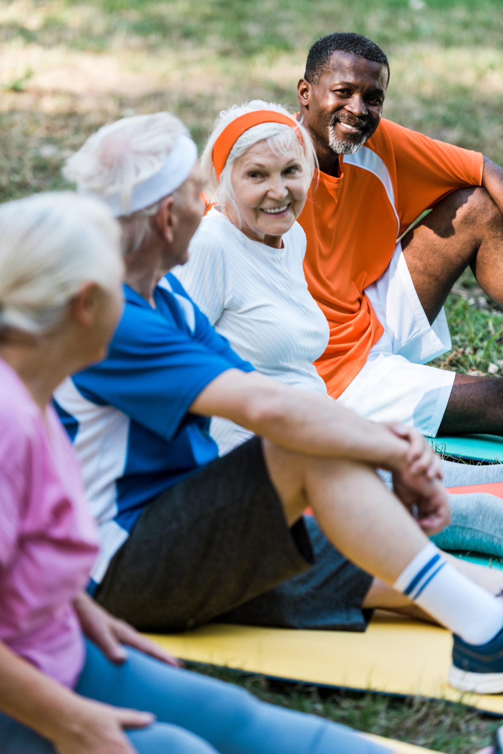 selective focus of cheerful multicultural men and women in sportswear sitting on fitness mats